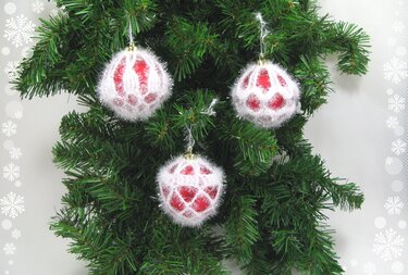 Drei rote Weihnachtskugeln mit weißen gehäkelten Hüllen an Tannenzweigen