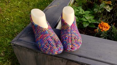 Mehrfarbige gestrickte Hausschuhe auf Schuhformern, Holzbank im Freien