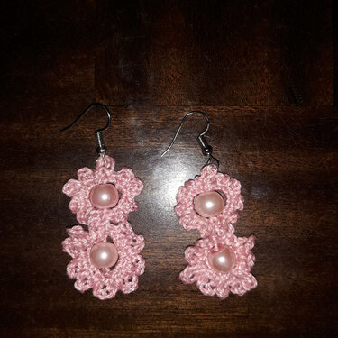 Rosa gehäkelte Ohrringe mit zwei Blüten und rosafarbenen Perlen auf dunklem Holz
