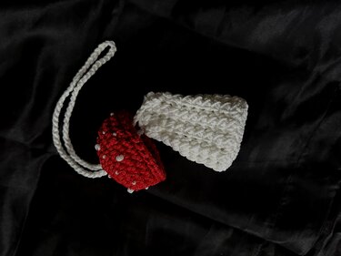 Two small crocheted drawstring pouches on black fabric
— one white textured pouch and one red beaded pouch with a braided cord