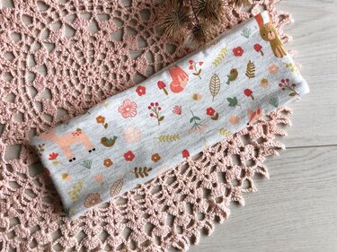 Hellgrauer Stoff mit Reh-, Hase- und Fuchsmotiven sowie Blumen und Pilzen auf rosa Häkeldecke