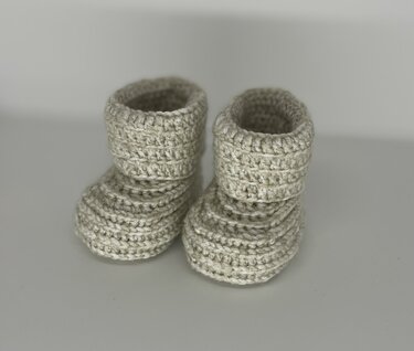 Nahaufnahme von zwei cremefarbenen gehäkelten Baby-Booties mit geripptem Muster und Umschlagbund.