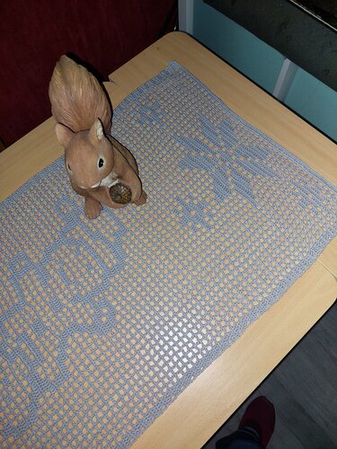 Hellblauer gehäkelter Tischläufer mit Filetmuster und keramischer Eichhörnchenfigur auf Holztisch