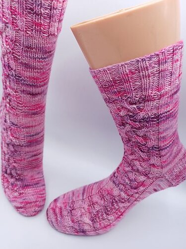 Handgestrickte, melierte rosafarbene Socken mit Zopfmuster auf Fußpuppe, Vorder- und Seitenansicht