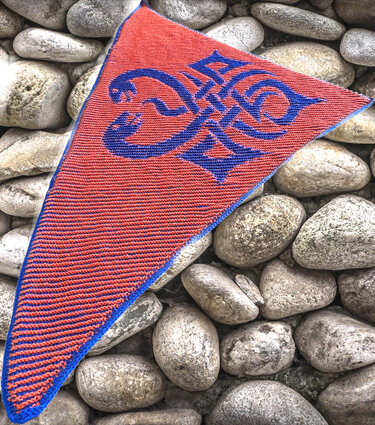 Rotes gestricktes Dreieckstuch mit blauem Zierknotenmotiv auf Flusssteinen