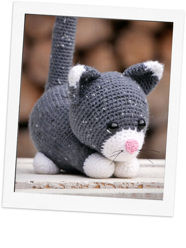 Gehäkelte graue Amigurumi-Katze mit weißen Pfoten und rosa Nase