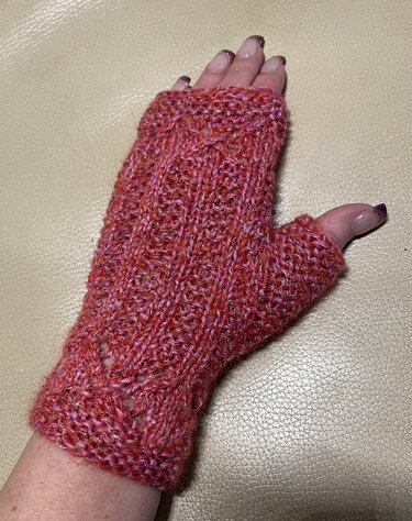 Gehäkelter, fingerloser Stulpen in Rot- und Pinktönen an einer Hand vor hellem Hintergrund.