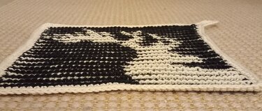 Schwarz-weißer gestrickter Topflappen, flach auf hellem Teppich liegend