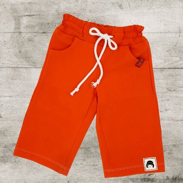 Orange Kinderhose mit elastischem Bund, weißer Kordel und seitlichen Taschen sowie kleinem Aufnäher