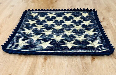 Gestrickter Teppich mit Sternenmuster in Dunkelblau und Creme auf Holzboden, mit gezackter Umrandung