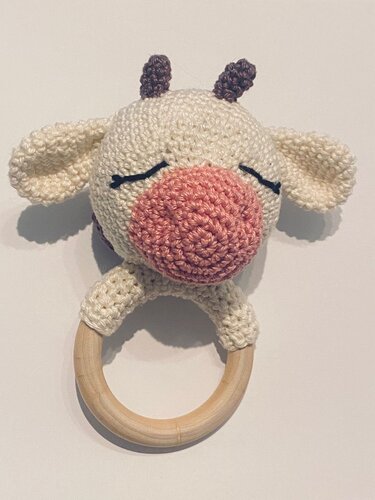 Hand-crocheted cream cow head with pink snout and closed embroidered eyes on a natural wooden ring.