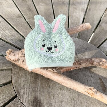 Mintgrüner Frottee-Waschhandschuh in Hasenform mit gesticktem Gesicht und rosa Ohren auf Holzuntergrund.