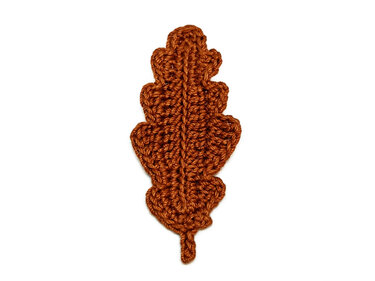 Brown crocheted oak leaf on a plain white surface, highlighting its handmade texture and intricate stitches.