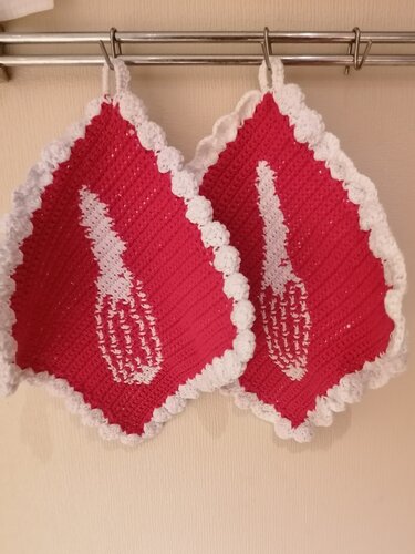 Zwei rote gehäkelte Topflappen mit weißer Muschelbordüre und Schneebesenmotiv hängen an einer Stange