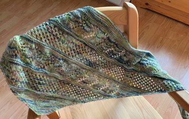 Elegantes gestricktes Dreieckstuch in Waldtönen mit Ajour- und Blattmotiven, locker über einen Holzstuhl gelegt