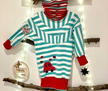 Detailansicht eines gestreiften Kinderpullovers mit roten Bündchen und roter Auto-Applikation, aufgehängt an einem Ast