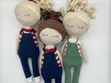 Nahaufnahme von drei gehäkelten Amigurumi-Puppen mit Fokus auf Augen, Latzhosen und Frisuren