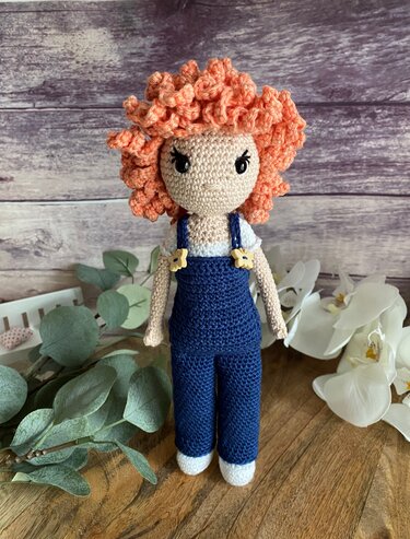 Handgehäkelte Amigurumi-Puppe mit kupferfarbenen Locken und blauer Latzhose