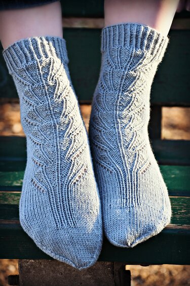 Paar grauer handgestrickter Socken mit Blattmuster auf einer Holzbank