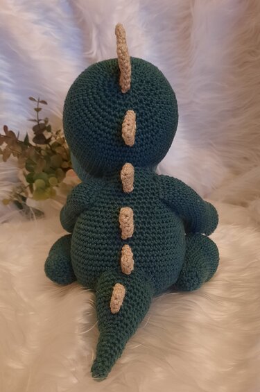 Rückansicht eines gehäkelten Amigurumi-Dinosauriers in Dunkelgrün mit beigen Stacheln