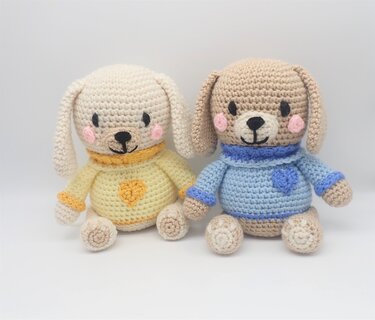 Front view of two small crocheted amigurumi puppies in yellow and blue sweaters, showing proportions and stitch details