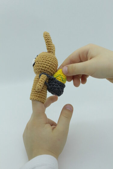 Gehäkelte Fingerpuppe Hase mit Körbchen und gelbem Ei an einem Finger