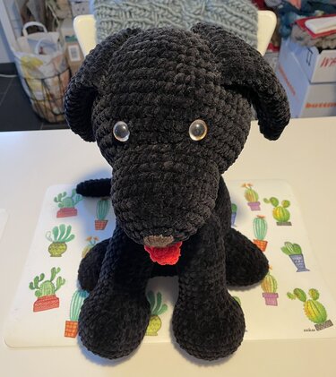 Plüschiger, gehäkelter schwarzer Hund mit roter Zunge und glänzenden Augen