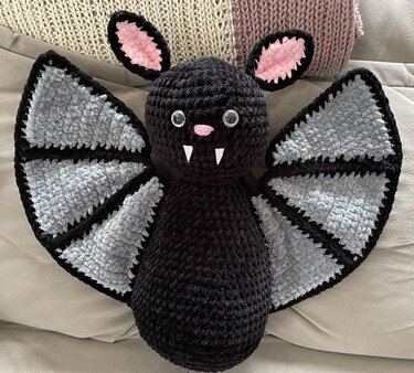 Schwarze gehäkelte Fledermaus mit grauen Flügeln, rosa Ohren und weißen Zähnchen