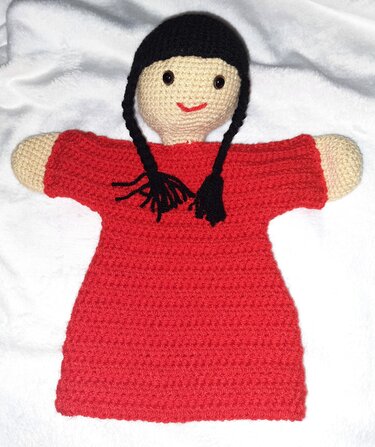 Gehäkelte Handpuppe in rotem Kleid mit zwei schwarzen Zöpfen