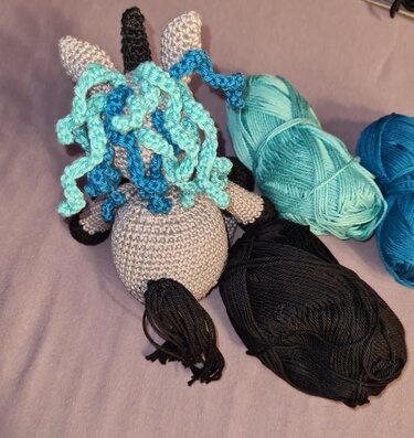 Gehäkelte spiralförmige Mähne aus türkis-blauen Garnsträngen am Einhornkopf mit schwarzen Garnknäueln