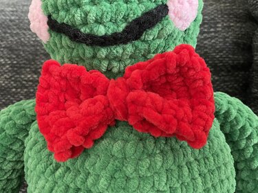 Gehäkelter grüner Amigurumi-Frosch mit roter Fliege und rosa Wangen