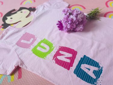 Rosa Kinder-T-Shirt mit bunten Blockbuchstaben L U N A und kleinem Blumenstrauß