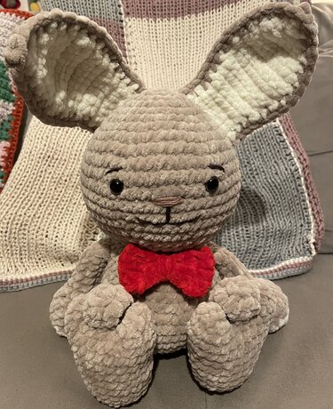 Nahaufnahme eines gehäkelten Amigurumi-Hasen mit großen Ohren und roter Fliege, Details von Kopf und Körper sichtbar