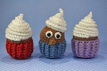 Drei gehäkelte Cupcake-Figuren mit weißer Cremehaube in Rot, Blau und Lila, eine mit Kulleraugen und gehäkelter Nase