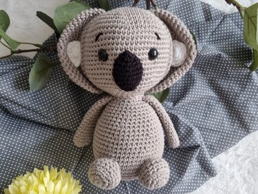 Beiger gehäkelter Koala-Amigurumi mit schwarzer Nase auf gepunktetem Stoff