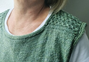 Grünes, ärmelloses Stricktop mit Strukturmuster an der Schulter; darunter ein weißes T‑Shirt.