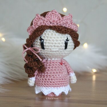 Gehäkelte Amigurumi-Puppe in rosa Kleid mit weißem Saum, braunem Zopf und rosa Krone