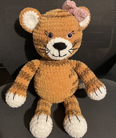 Gehäkeltes Amigurumi-Tiger Kuscheltier in orange-braun mit weißen Pfoten und rosa Schleife