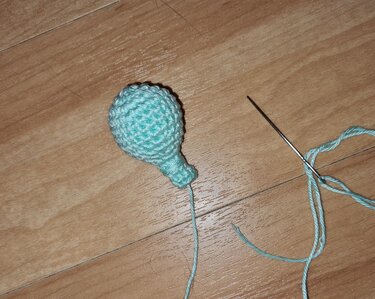 Hellblaues gehäkeltes Amigurumi-Teil mit Stopfnadel auf Holzoberfläche