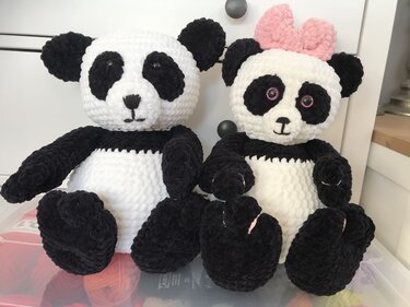 Zwei weiß-schwarze, handgehäkelte Panda-Amigurumis nebeneinander; rechts mit rosa Schleife und rosa Augenumrandung.