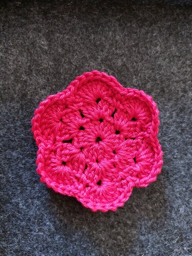 Sechspetalige gehäkelte Blüten-Applikation in Pink auf dunkelgrauem Hintergrund