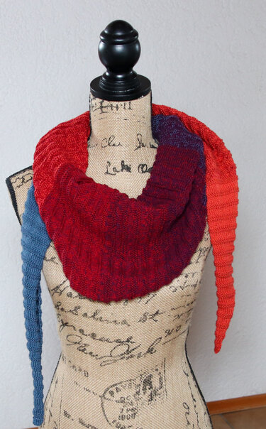 Gestricktes Dreieckstuch mit rotem Mittelteil und blauen sowie orangen Zipfeln auf Schneiderpuppe