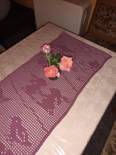 Handgehäkelter lila Tischläufer mit Herzmuster und drei rosafarbenen Rosen.