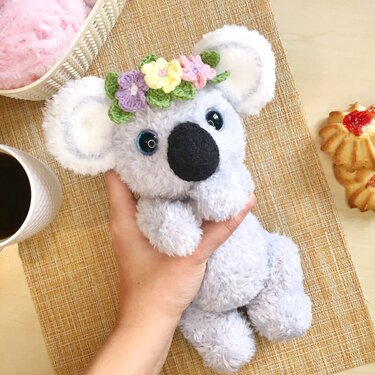 hand holding a gray crocheted koala amigurumi wearing a pastel flower crown