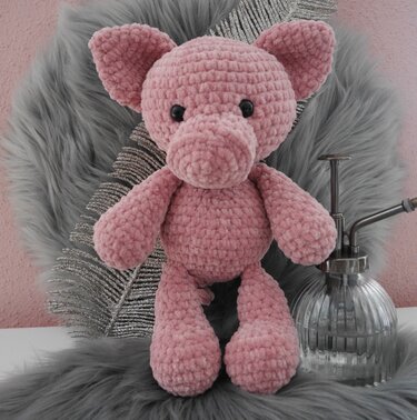 Rosa Amigurumi‑Schweinchen in flauschiger Optik auf grauem Untergrund