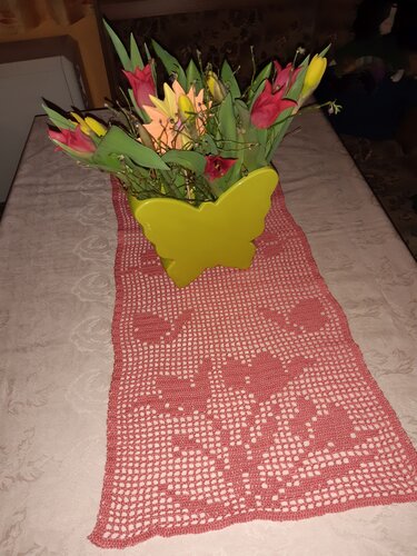 Frühlingshaft gedeckter Tisch mit lachsfarbenem gehäkeltem Läufer und buntem Tulpenstrauß in gelber Schmetterlingsvase.