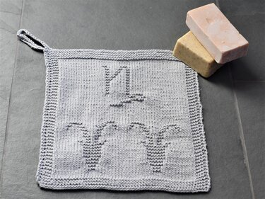 Light grey knitted square washcloth with textured candle motif and hanging loop