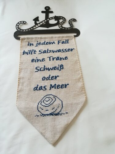 Heller Stoffwimpel mit blauem Kreuzstich‑Spruch und Muschelmotiv an Anker‑Halterung