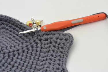 Gehäkelte graue Fläche mit orangefarbener Häkelnadel 5,0 mm und Perlen-Maschenmarkierer