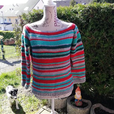 Gehäkelter Damenpullover mit roten, türkisen, grünen und grauen Querstreifen auf einer Schneiderbüste im Garten
